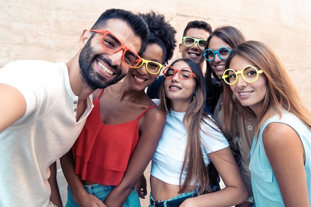 Grupo de adolescentes tirando uma selfie engraçada usando óculos de sol coloridos estranhos