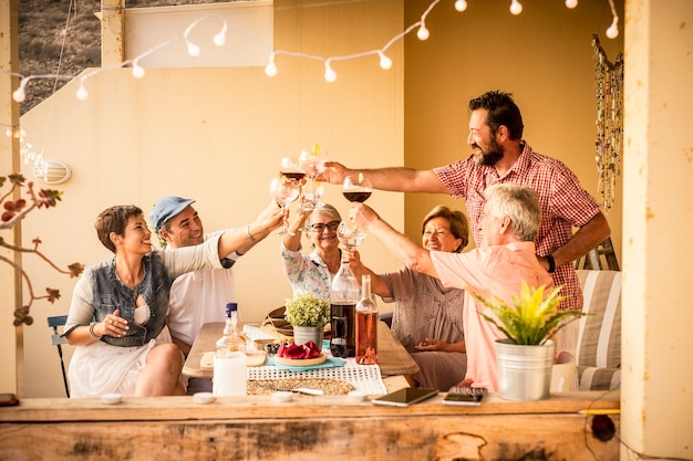 Grupo de adultos mistos com idades entre 40 e 80 anos festejam juntos em casa no terraço com comida e vinho