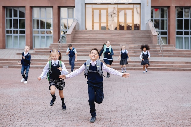 Grupo de alunos de uniforme está descendo as escadas correndo para fora da escola.