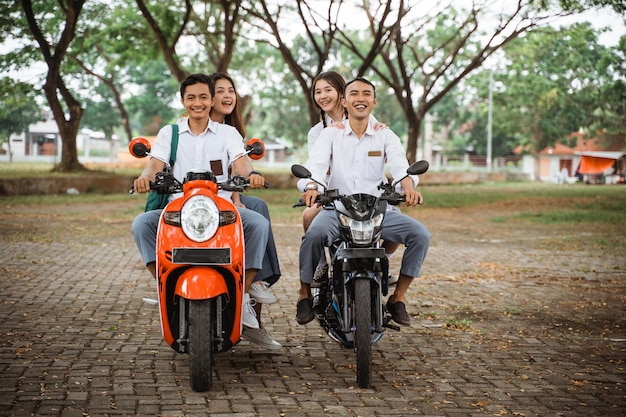 Foto grupo de alunos do ensino médio em uniforme montando motocicleta sem capacete no parque