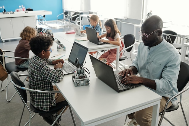 Grupo de alunos interculturais e seu professor usando laptops na aula