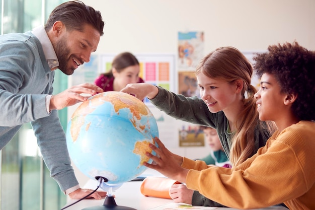 Grupo de alunos multiculturais com professores em sala de aula olhando para o globo na aula de geografia