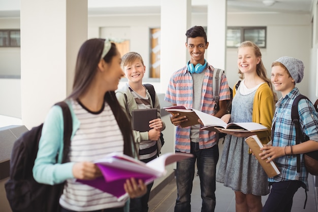 Grupo de alunos sorridentes em pé com o caderno no corredor