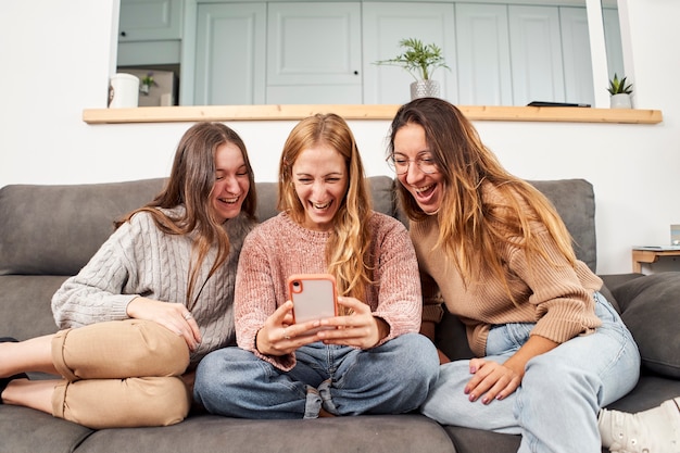 Grupo de amigas no sofá em casa, usando um telefone celular rindo