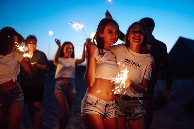 Grupo de amigos à noite na praia com estrelinhas Jovens amigos desfrutando de férias na praia