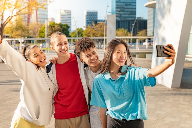 Grupo de amigos adolescentes felizes tirando uma selfie com o telefone e rindo na rua da cidade