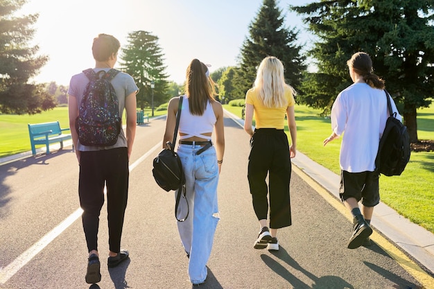 Grupo de amigos adolescentes no dia ensolarado de verão caminhando juntos na estrada vista traseira