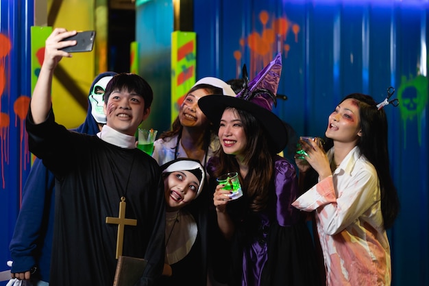 Grupo de amigos asiáticos descansa em uma boate com coquetéis coloridos vestindo fantasias de Halloween na festa na boate, fazendo caras assustadoras. Comemoração do Dia das Bruxas