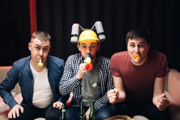 Grupo de amigos assiste TV em casa Seu time marca o gol e ganha a torcida dos jovens Três amigos homens felizes descansando à noite em casa com cerveja e torcendo por um gol