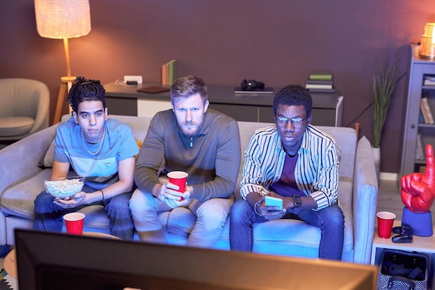 Grupo de amigos assistindo TV em casa e comendo lanches iluminados por luz azul