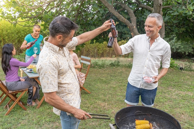 Grupo de amigos brindando ao redor do churrasco sorrindo pessoas bebendo no pátio