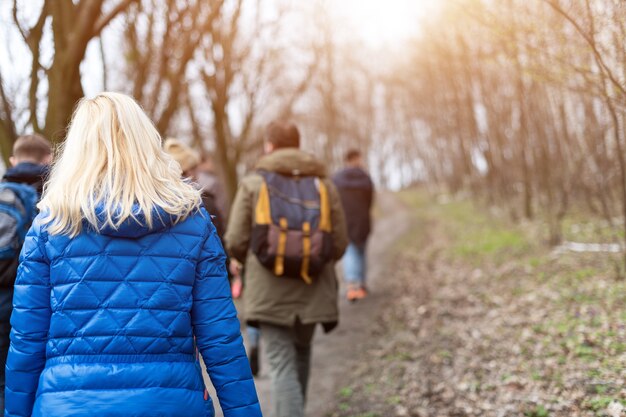 Grupo de amigos caminhando com mochilas na floresta da primavera, nos fundos