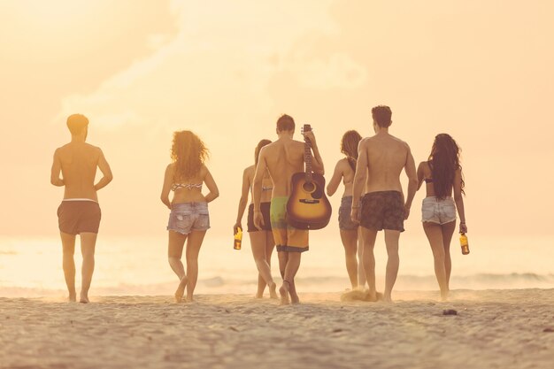 Grupo de amigos, caminhando na praia ao pôr do sol.