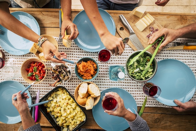 Grupo de amigos comendo junto com um copo de vinho na mesa de jantar. mãos tirando comida da tigela no prato. grupo de pessoas desfrutando de uma variedade de comidas e bebidas em uma festa em grupo