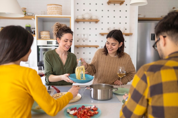 Foto grupo de amigos comendo macarrão juntos na cozinha