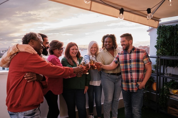 Grupo de amigos de diversas culturas reunidos brindando com cerveja no terraço conceito juntos divertido