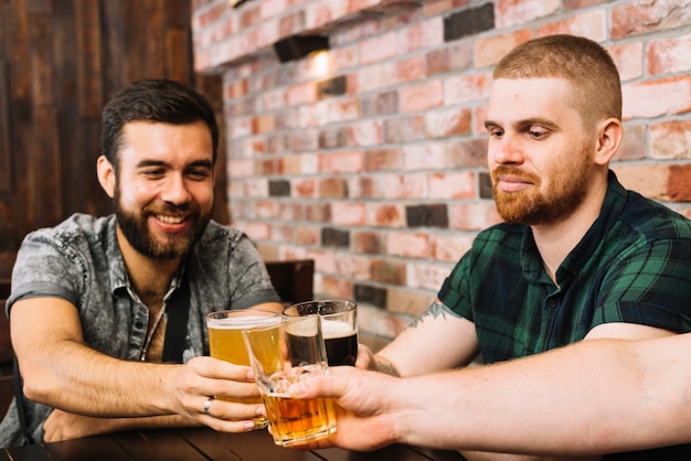 Grupo de amigos do sexo masculino brindando copos alcoólicos em bar