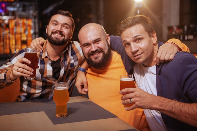 Foto grupo de amigos do sexo masculino felizes sorrindo para a câmera enquanto bebia cerveja juntos no bar