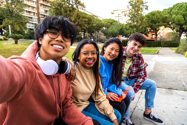 Grupo de amigos estudantes universitários multirraciais tirando selfie com telefone do lado de fora estudantes rindo e se divertindo no parque