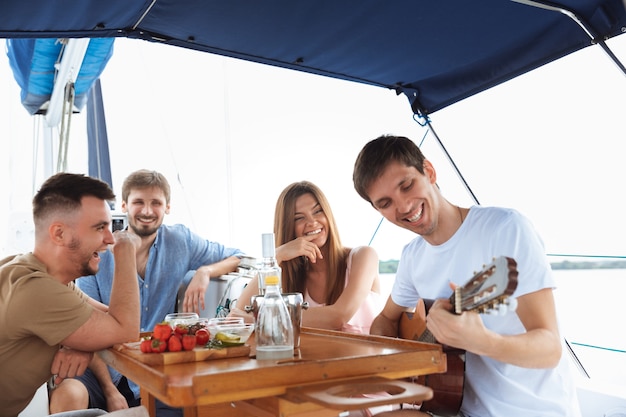 Grupo de amigos felizes bebendo coquetéis de vodka na festa do barco ao ar livre, alegre e feliz. jovens tocando violão no conceito de passeio, juventude e férias de verão do mar. álcool, férias, descanso.