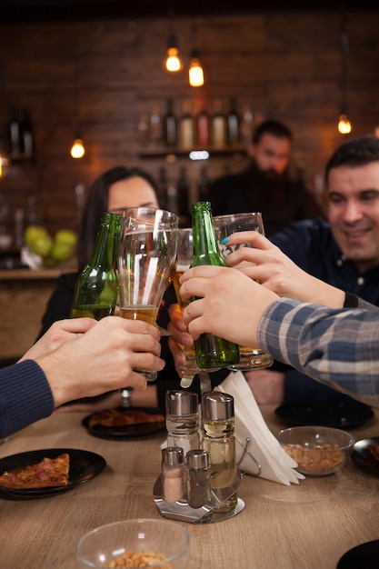 Grupo de amigos felizes bebendo e brindando cerveja no restaurante-bar da cervejaria. Celebração da amizade.