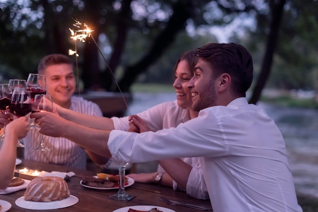 grupo de amigos felizes brindando com copo de vinho tinto enquanto fazia piquenique jantar francês ao ar livre durante as férias de verão perto do rio na bela natureza