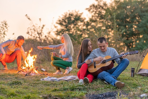 Grupo de amigos felizes com guitarra, se divertindo ao ar livre, perto da barraca da fogueira e do turista. Diversão de acampamento família feliz