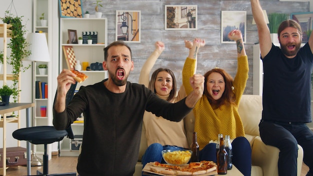 Grupo de amigos felizes depois que seu time de futebol favorito vence o campeonato. Amigos sentados no sofá comendo pizza e batatas fritas.