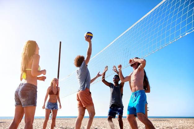 Grupo de amigos felizes jogando vôlei de praia na praia