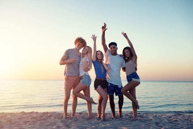 Grupo de amigos felizes se divertindo na praia ao amanhecer