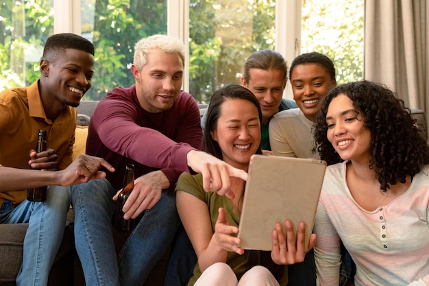 Grupo de amigos femininos e masculinos felizes, bebendo cerveja juntos e usando tablet