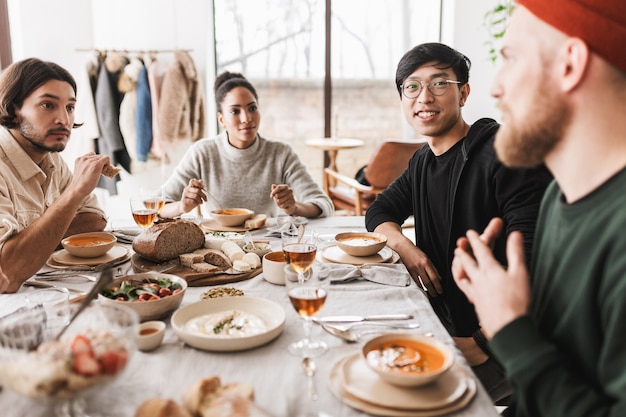 Grupo de amigos internacionais sentado à mesa cheia de comida conversando sonhadoramente