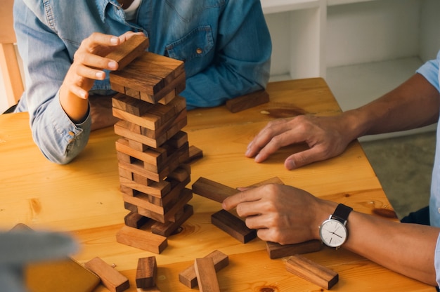 Grupo de amigos jogando o jogo de blocos de madeira na mesa quebra-cabeça dobrado segurando o jogo de blocos de madeira Risco de planejamento e estratégia nos negócios