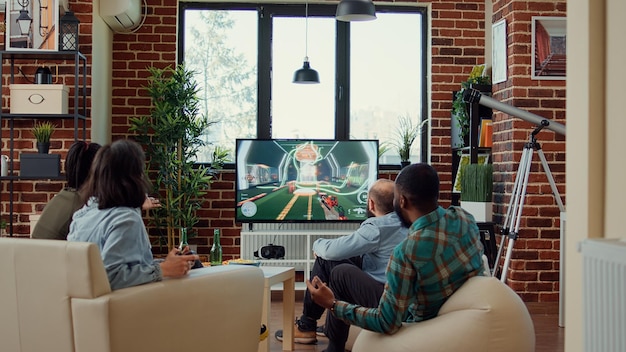 Grupo de amigos jogando videogame no console, aproveitando o desafio de jogos na televisão com joystick. Pessoas se divertindo com a competição online e jogabilidade no hangout da festa.
