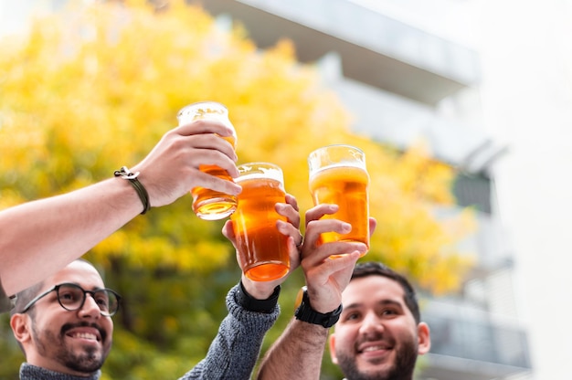 Foto grupo de amigos latinos brindando e sorrindo, levantando seus copos de cerveja artesanal, do lado de fora de um bar em um dia de outono. estilo de vida e conceito de bar.