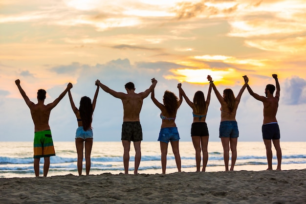 Grupo de amigos, levantar as mãos na praia ao pôr do sol