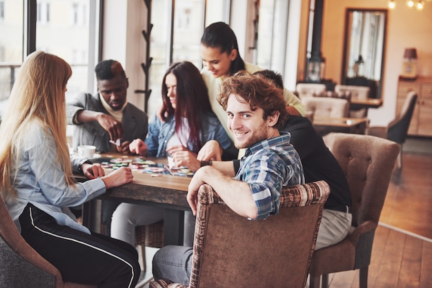 Grupo de amigos multiétnicos criativos, sentado à mesa de madeira. Pessoas se divertindo enquanto jogava jogo de tabuleiro