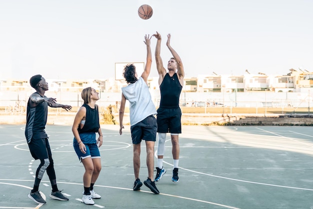 Grupo de amigos multiétnicos pulando enquanto jogava basquete em uma quadra ao ar livre durante o pôr do sol