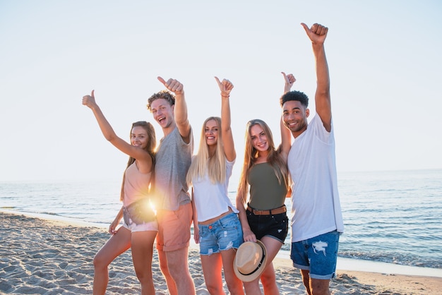 Grupo de amigos na praia com o polegar levantado