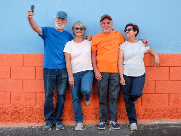 Grupo de amigos ou família em pé contra uma parede colorida - quatro idosos - conceito de ativo com aposentados