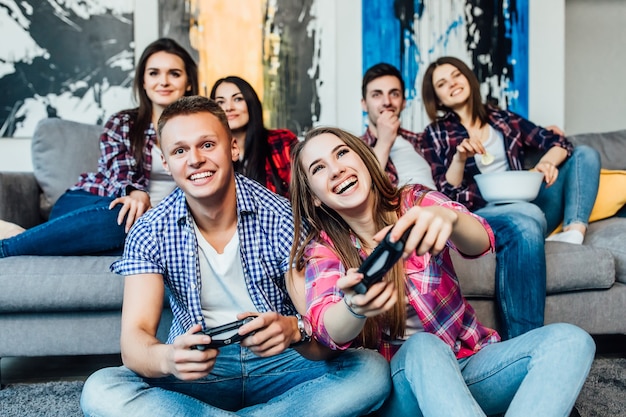 Grupo de amigos se divertindo jogando videogame, sentado no sofá em casa. Conceito sobre tecnologia, videogames, estilo de vida e pessoas