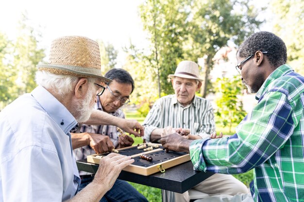 Grupo de amigos sênior jogando xadrez no parque. Conceitos de estilo de vida sobre antiguidade e terceira idade