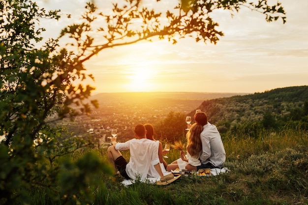 Grupo de amigos sentado na montanha e apreciando a paisagem incrível e o pôr do sol.