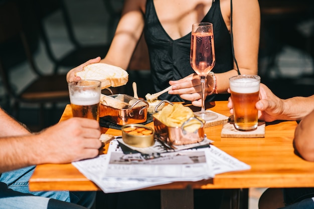 Grupo de amigos sentados em um terraço de verão com cerveja e vinho nas mãos e petiscos na mesa