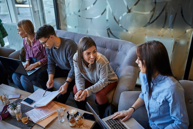 Grupo de amigos sentados juntos em um café com laptop e documentos