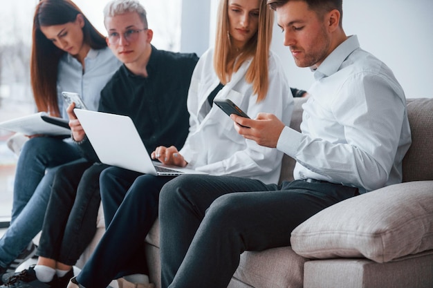 Grupo de amigos sentados no sofá com laptop e telefones juntos