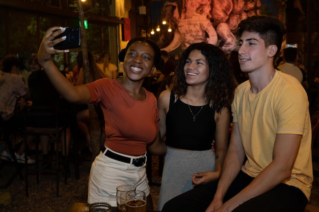 Grupo de amigos tirando auto-retrato em bar com flash. Conceito multiétnico