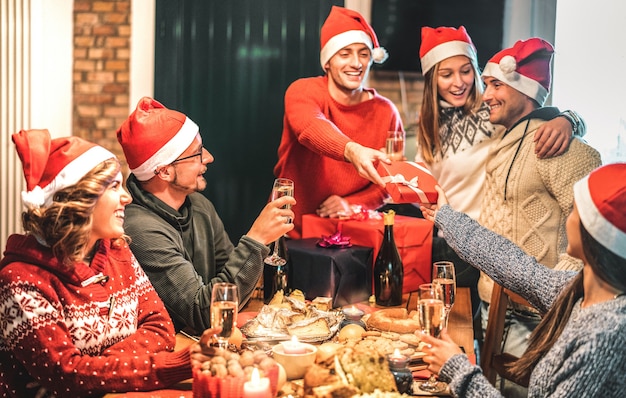 Grupo de amigos usando chapéu de papai noel dando presentes de natal uns aos outros