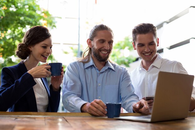 Grupo de amigos usando laptop enquanto tomando café