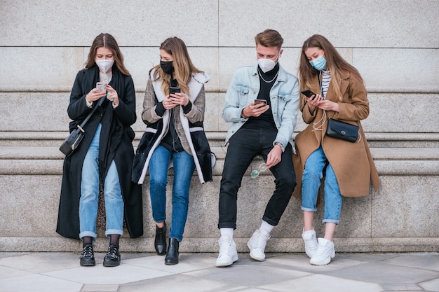 Foto grupo de amigos usando máscara facial e usando seus smartphones